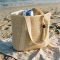 Bolso Médano tejido con flecos color beige, sobre una toalla en la playa