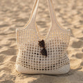 Bolso Médano tejido blanco de malla calada, sobre la arena al atardecer