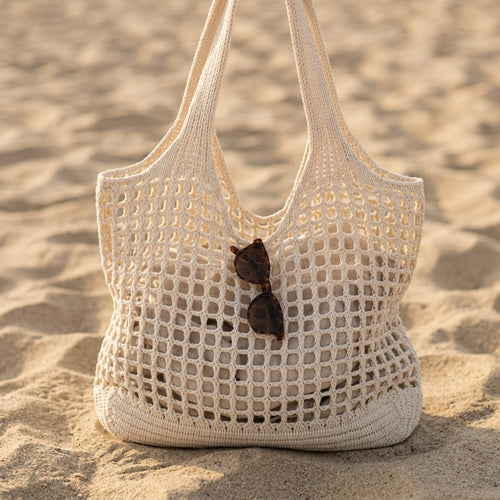 Bolso Médano tejido blanco de malla calada, sobre la arena al atardecer